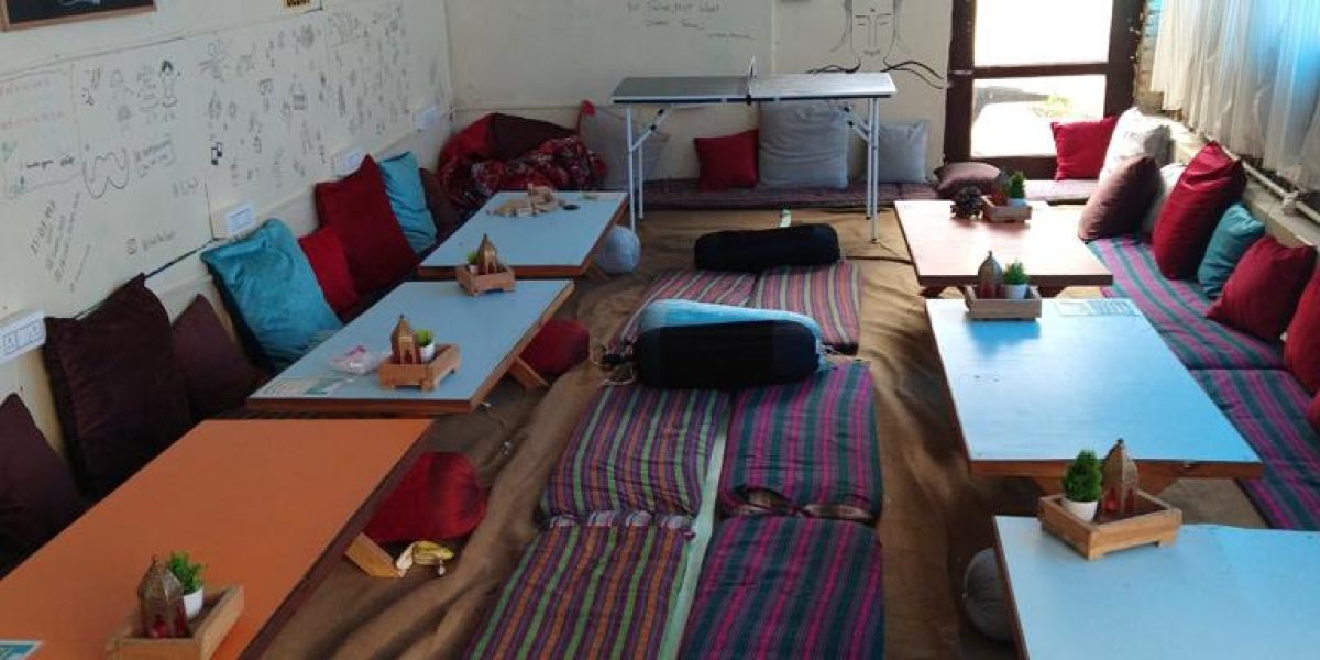 Cozy gathering room in a North Indian hostel, featuring colorful floor seating, low tables, and a laid-back atmosphere perfect for travelers seeking authentic experiences and connection.